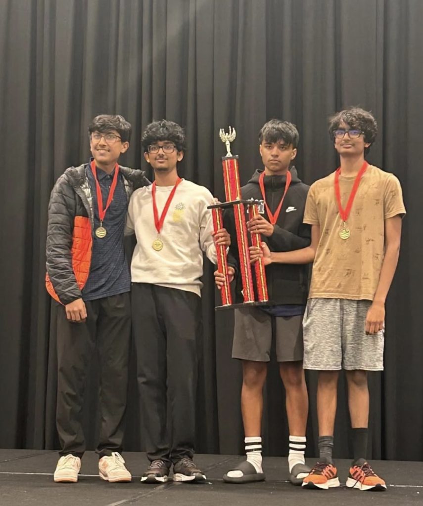 Four students holding a trophy and wearing medals on stage at the High School National Championship Tournament
